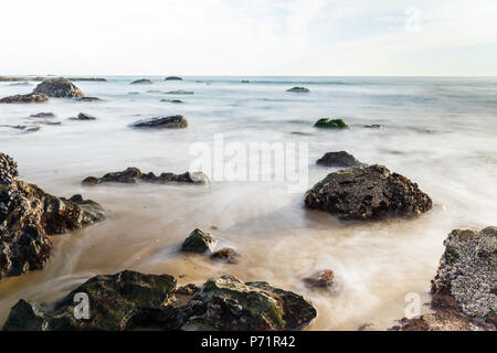 The sandy beach of Crystal Cove State Park in Laguna beach, California is littered with exposed rocks at low tide in the late afternoon. Stock Photo