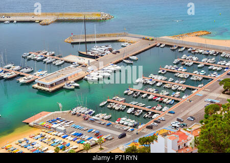 Sea port with boat berths and concrete promenade. Private yachts and fishing boats are moored at the pier. Coast of Spanish beach resort Blanes in sum Stock Photo