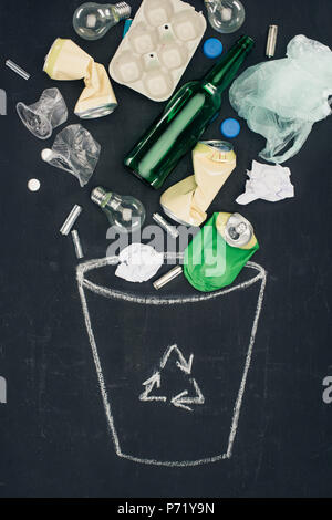various types of trash falling into drawn trash can with recycle sign on chalkboard Stock Photo
