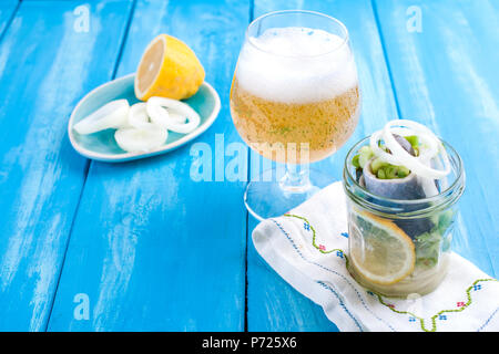 Traditional Dutch marinated herring with lemon and onions in a jar. Fresh Belgian beer in a glass. Seafood on a blue background. Copy sapce Stock Photo