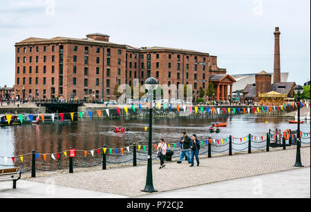 People at Salthouse Dock with Albert Dock converted warehouse and brick tower and people walking looking at phones, Liverpool, England, UK Stock Photo