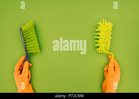 cropped image of woman holding two different cleaning brushes in hands isolated on green Stock Photo