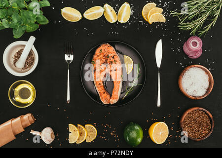 top view of salmon steak with cutlery and seasonings on black Stock Photo