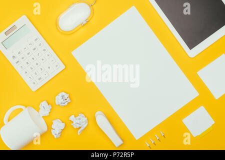 top view of blank sheet of paper, crumpled papers, notes, calculator and cup isolated on yellow Stock Photo