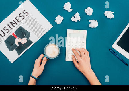 cropped shot of person using calculator and drinking coffee on blue Stock Photo