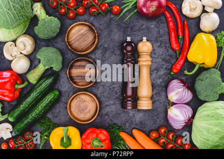 top view of fresh organic vegetables, wooden plates and containers for spices on black Stock Photo