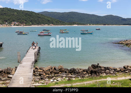 Florianópolis, Santa Catarina, Brazil. Beautiful view of wooden pier with sea and colorful fishing boats in background on sunny summer day with sea in Stock Photo