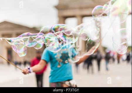 Colorful soap bubbles floating in the foreground. Street performer, busker, entertaining the crowd in front of the Brandenburg Gate in Berlin. Stock Photo