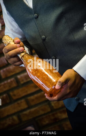 stylish man groom holding golden bottle of champagne. luxury wedding reception. catering and service at restaurant. space for text Stock Photo