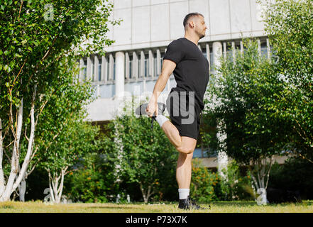 Attractive man doing stretching legs exercises with hands in park. Stock Photo