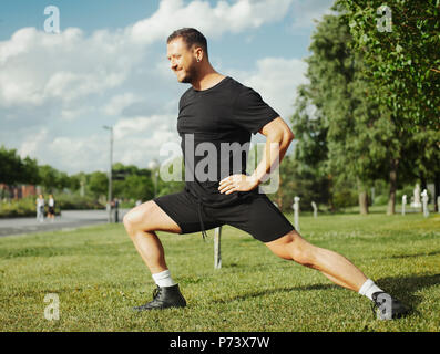 Young attractive man doing lunge outdoor in the park. Side view. Stock Photo