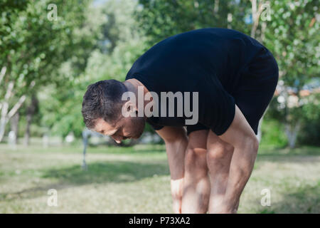 Attractive man doing stretching exercises outdoors in park. Stock Photo