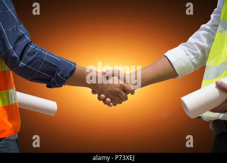 Handsome construction workers in protective helmets and vests are shaking hands while working in the office center, Horizontal, Blurred background Stock Photo