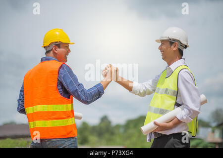 Handsome construction workers in protective helmets and vests are shaking hands while working on construction site Stock Photo