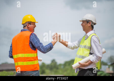 Handsome construction workers in protective helmets and vests are shaking hands while working on construction site Stock Photo