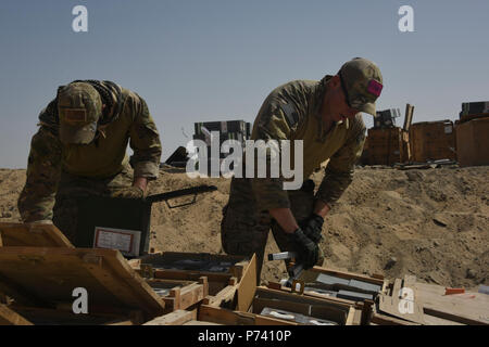 Two Explosive Ordnance Disposal technicians with the 386th Expeditionary Civil Engineer Squadron, place flares inside wooden crates during an ammunition disposal request burn operation at an undisclosed location in Southwest Asia, May 11, 2017. The stockpile of expired munitions consisting primarily of flares was transported to an isolated location where the unserviceable items were stacked in a man-made hole in preparation for destruction. Stock Photo