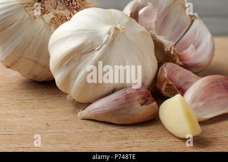 Garlic bulbs and cloves, one of them peeled and cut in half, on old scratched cutting board. Stock Photo