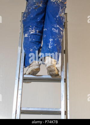 Legs of a person wearing a blue paint-stained overall standing on a ladder image with copy space in portrait format Stock Photo