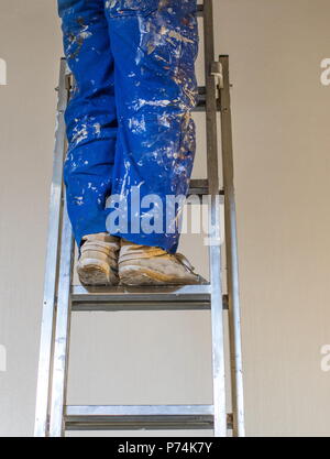 Legs of a person wearing a blue paint-stained overall standing on a ladder image with copy space in portrait format Stock Photo