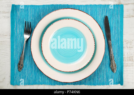 Top view of a pair of empty salad and dinner plates with a teal blue well and vintage fork and knife on a turquoise napkin and white painted wooden ta Stock Photo