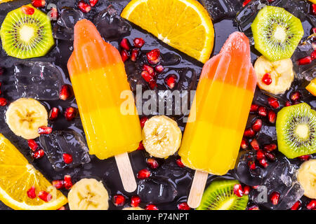 Fruit ice cream on stick with slices fruits on black slate board. Focus on Popsicles. Stock Photo