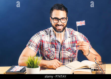 Eastern bearded man holding English flag at the working table with books, successful language learning concept, studio isolated background Stock Photo