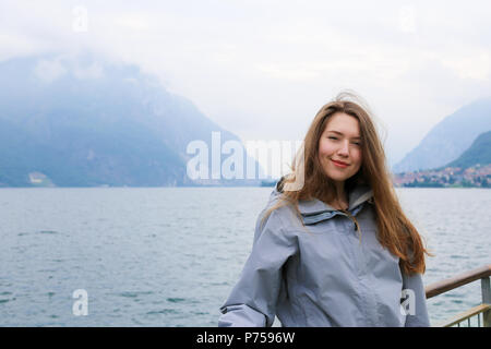 Young caucasian woman standing near banister, lake Como and Alps mountain in background. Stock Photo