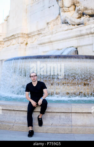 Young businessman sitting near Trevi fountain, wearing glasses and black clothes. Stock Photo