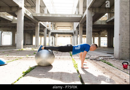 Young handsome athlete man doing pushups with silver pilates ball  in an old abandoned building Stock Photo