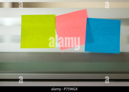 Three colored sticky notes over glass screen of a bench desk Stock Photo