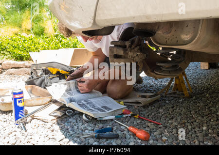 DIY car maintenance and repairs - young man reading Haynes manual as he changes the brake pads, brake disc and brake caliper for the first time Stock Photo