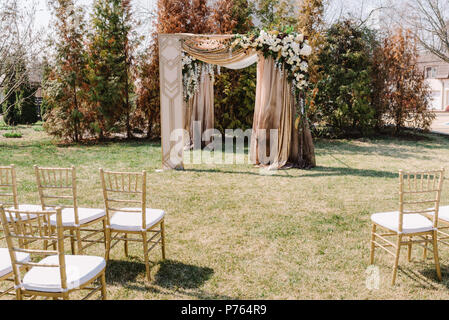 Magnificent wedding arch for a wedding ceremony. The square arch decorated by golden fabric and flowers Stock Photo