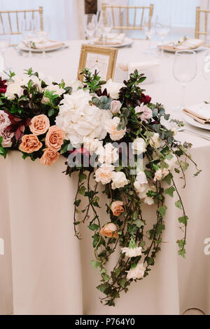 Decoration of a wedding table of newlyweds greens and in flowers. Long, hanging on a table, composition from are fresh flowers Stock Photo