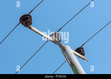 Close up of overhead power cables and insulators at the top of a pole, against a blue sky Stock Photo