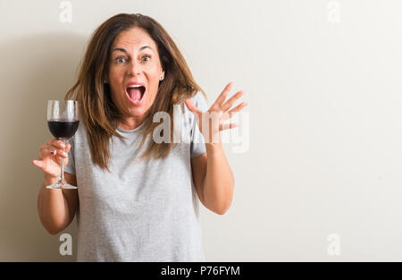 Middle age woman drinking red wine in a glass very happy and excited, winner expression celebrating victory screaming with big smile and raised hands Stock Photo