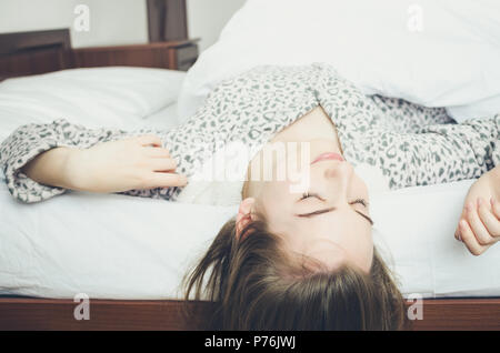 Happy young woman enjoying sunny morning. Caucasian girl in cute warm pajamas stretching in the bed and smiling after waking up. Good start of the day Stock Photo