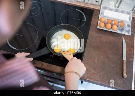 Anonymous young man standing in kitchen and preparing eggs for breakfast while spending time alone. Stock Photo