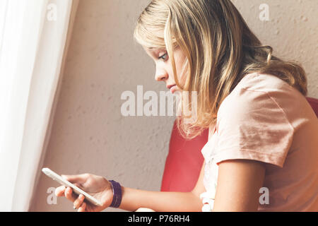 Shocked European blond teenage girl in pink t-shirt with a smartphone, indoor closeup profile portrait Stock Photo