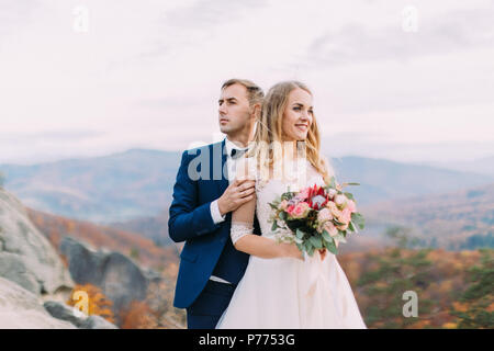 Close-up horizontal portrait of the newlyweds looking at different sides at the blurred background of the yellowed nature. Stock Photo