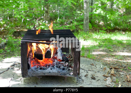 A camp site fire pit is lit, burning with glowing coals and ember on a sunny day Stock Photo