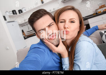 Young couple man and woman together at home taking photos making duck face grimace funny Stock Photo