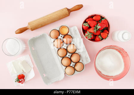 Flat lay raw ingredients for cooking strawberry pie or cake on pink background  (eggs, flour, milk, sugar, strawberry), top view. Bakery background. R Stock Photo