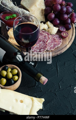 Bottle of red wine with wine glass and antipasti. Assorted Italian style banquet food set. Delicious snack on party. Board with salami, bread, sauce,  Stock Photo
