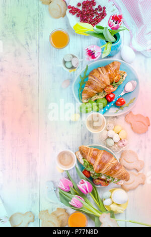 Easter breakfast. A family breakfast of croissants with rocket salad and cheese and aromatic coffee. Fresh tulips of pink color and eggs of different colors and Easter decor. Free space for text Stock Photo