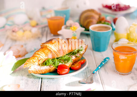 A family breakfast of croissants with rocket salad and cheese and aromatic coffee. Fresh tulips of pink color and eggs of different colors and Easter decor, ceramic rabbits. Free space for text. Stock Photo