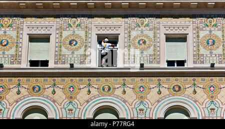 Workman wearing a harness, cleaning windows glasses. Dangerous work. Government Building, Unity Square. Palazzo del Governo.Trieste, Italy, Europe. Stock Photo