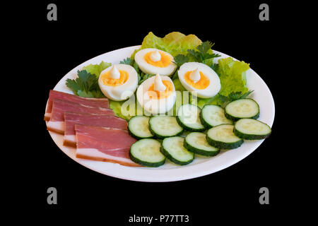breakfast. Boiled eggs, bacon, greens in a white plate isolated on a black background. Stock Photo