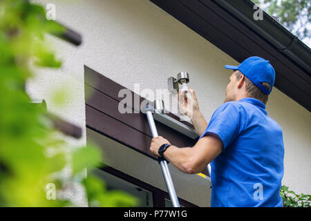 electrician standing on ladder and change the light bulb in house facade lamp Stock Photo