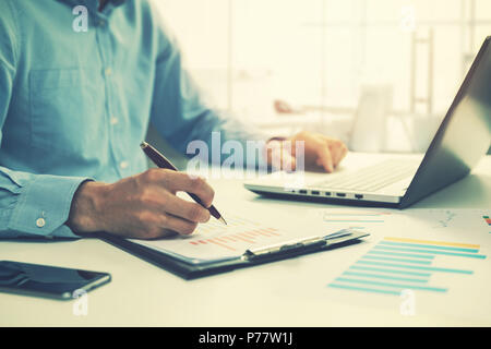 businessman analyzing annual business report and using laptop at office desk Stock Photo