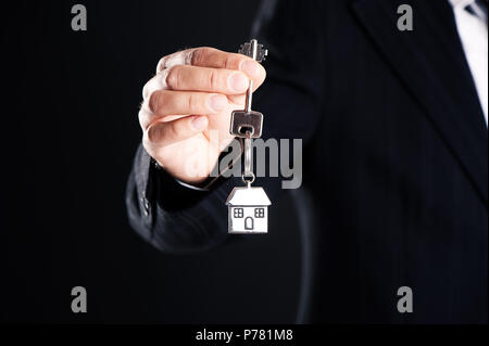 cropped image of man holding key from house isolated on dark background Stock Photo